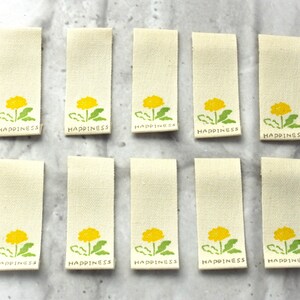 May include: Ten white fabric labels with a yellow dandelion design and the word "Happiness" printed in green.