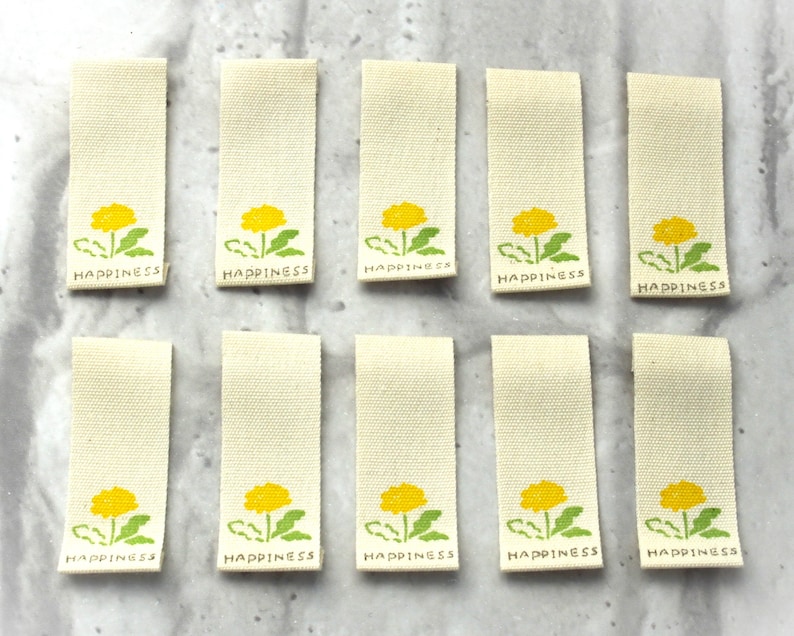 May include: Ten white fabric labels with a yellow dandelion design and the word "Happiness" printed in green.