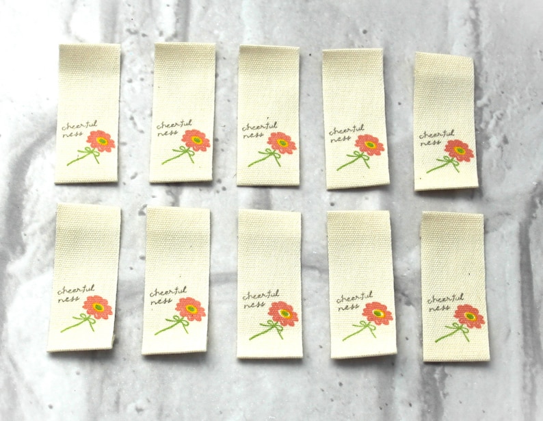 May include: Ten off-white fabric tags with a pink flower and the text "cheerfulness" printed on each.