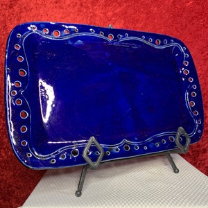 May include: A rectangular, deep blue ceramic serving tray with a glossy finish. The tray has a decorative border with small, evenly spaced holes and a white accent line. It is displayed on a black metal stand.