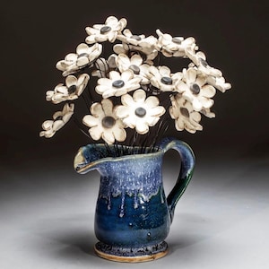 May include: A blue ceramic pitcher with a white glaze and a bouquet of white ceramic flowers with black centers.