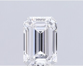 May include: A clear, emerald-cut diamond with a rectangular shape and faceted surfaces. The gemstone reflects light, showcasing its brilliance and clarity. The diamond is set against a plain, light background, highlighting its features.