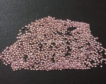 May include: A large collection of small, round, light pink gemstones scattered across a dark, textured surface. The gemstones are uniform in size and shape, reflecting light. The image is well-lit, highlighting the sparkle of the gems. The overall effect is one of abundance and luxury.