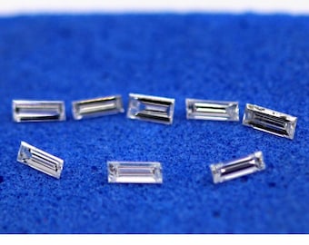 May include: A collection of small, rectangular-cut diamonds, each with multiple facets, are displayed on a textured blue surface. The diamonds are clear and reflect light, showcasing their brilliance. Ideal for jewelry making.