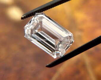 May include: A clear, rectangular emerald cut diamond held by tweezers. The diamond is faceted and reflects light.