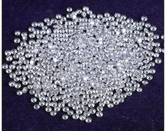 May include: A collection of small, round, clear gemstones scattered on a dark blue surface. The gemstones are highly reflective, catching the light and creating a sparkling effect. The overall impression is one of luxury and brilliance.