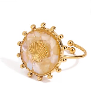 May include: Gold-toned adjustable ring featuring a circular design with a mother-of-pearl inlay and a gold seashell accent. The ring has a delicate band and is adorned with small, round embellishments around the outer edge of the circular design.