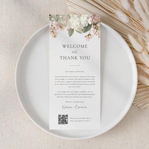 May include: A rectangular white card featuring a floral illustration of white and pink flowers at the top. The text reads Welcome and Thank You, followed by a message to family and friends, the names Danica and Cameron, and a QR code at the bottom.