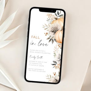 Pode incluir: Um smartphone preto exibe um convite com tema de outono com o texto "Fall in love". O design apresenta abóboras, flores e folhagens em tons neutros. O telefone repousa sobre uma superfície branca com uma folha de palmeira.