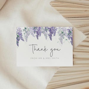 May include: A rectangular white thank you card featuring a watercolor illustration of purple wisteria flowers hanging from the top edge. The text reads Thank you in a black script font, followed by the text FROM MR & MRS SMITH in black.
