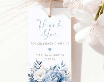 Può includere: Un'etichetta bianca con le parole "Thank You" in corsivo azzurro. L'etichetta include il testo "FOR CELEBRATING WITH US", un cuore blu e i nomi "MARINA & MARTIN" con una data. Il fondo presenta accenti floreali blu.