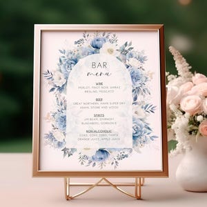 May include: A rectangular bar menu sign in a rose gold frame on a wire stand. The sign features a white arch background with blue and white floral illustrations. Text includes BAR menu, WINE, BEER, SPIRITS, and NON-ALCOHOLIC with various drink names.