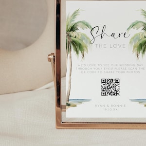 May include: A gold-framed sign with a white background and a tropical palm tree design. The sign says "Share the Love" and includes a QR code with the text "We'd love to see our wedding day through your eyes! Please scan the QR code to share your photos." The sign also includes the names "Ryan & Bonnie" and the date "19.10.XX".