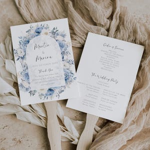 May include: Two wedding fan programs with wooden handles. One features the names "Martin & Marina" with a floral design in blue and white. The other lists the order of service and wedding party details.