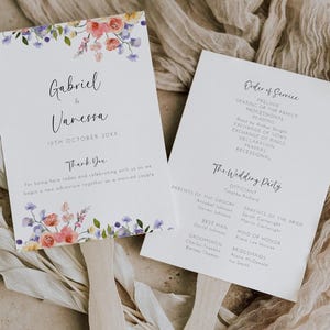 May include: Two white wedding programs with floral borders. One displays the names "Gabriel & Vanessa" and the date "19th October 20XX". The other lists the order of service and wedding party details.