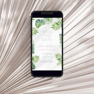 May include: A smartphone displays a wedding invitation with a tropical theme. The invitation features green watercolor leaves and the text "SAVE THE DATE" along with the names "Jodie and Austin" and the date "10.10.24". The background is a light, textured surface.