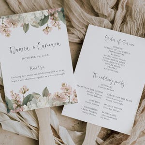 Peut inclure: Deux éventails de programme de mariage blancs avec des poignées en bois. La carte de gauche présente des illustrations florales roses et blanches, les noms Danica & Cameron et la date du 19 octobre 20XX. La carte de droite liste le déroulement.