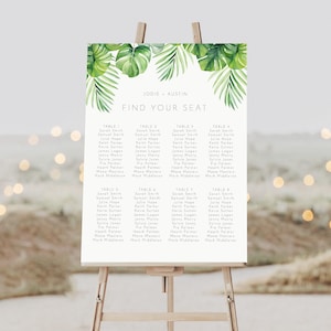 May include: A white wedding seating chart with a tropical theme. The chart features a green watercolor design of palm leaves and the text "Jodie & Austin Find Your Seat". The chart lists the names of guests assigned to each table.