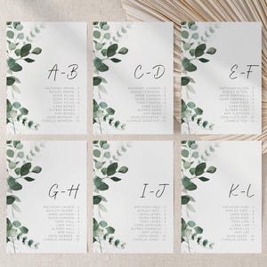 Könnte beinhalten: Sechs weiße Tischkarten für Hochzeiten mit Eukalyptusblatt-Design. Jede Karte hat eine Buchstabenpaarung, wie z. B. A-B, und eine Liste mit Namen. Die Karten sind auf einer neutralen Oberfläche mit einem getrockneten Palmblatt angeordnet.