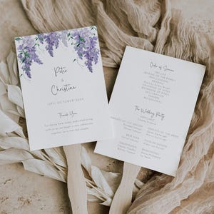 May include: Wedding ceremony program fan with a watercolor design of purple wisteria flowers. The fan includes the names "Peter & Christine" and the date "19th October 20XX". The back of the fan lists the order of service and the wedding party.