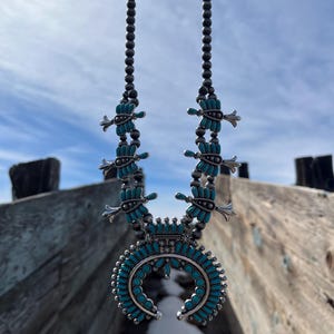 May include: A turquoise and silver Native American style necklace with a crescent moon pendant. The necklace is made of small turquoise beads and silver beads. The pendant is a crescent moon shape with a turquoise inlay.