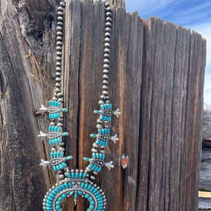 May include: A turquoise and silver Native American necklace with a crescent moon pendant. The necklace is made of turquoise beads and silver beads, and the pendant is a crescent moon shape with a turquoise stone in the center.