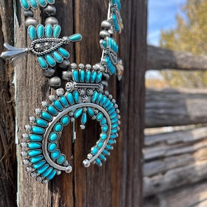 May include: A turquoise and silver Native American necklace with a crescent moon pendant. The necklace is made of turquoise stones and silver beads.