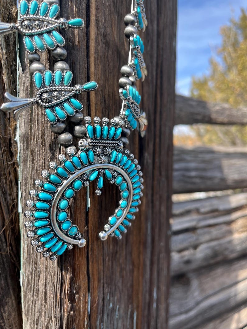 May include: A turquoise and silver Native American necklace with a crescent moon pendant. The necklace is made of turquoise stones and silver beads.