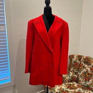 May include: A vibrant red double-breasted coat displayed on a black mannequin. The coat features a classic notched collar, two rows of buttons, and a tailored fit. The coat is a solid, bright red color.
