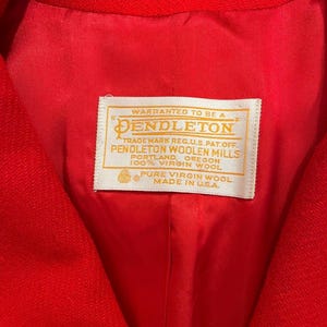 May include: Close-up of a bright red jacket interior. The lining is a matching red. A white label with gold lettering reads "Warranted to be a Pendleton" and details about the wool and origin, "Made in U.S.A."