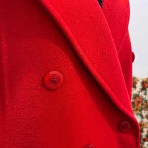 May include: Close-up of a bright red double-breasted blazer. The blazer features matching red buttons and a tailored lapel. The fabric has a subtle texture, and the overall design is classic and stylish.