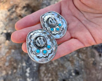 May include: A pair of silver earrings shaped like a sombrero with turquoise stones around the brim.