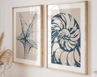 May include: Two framed prints with a beige background and blue illustrations of a starfish and a nautilus shell. The prints are hanging on a white wall above a wooden console table with books and a vase of dried flowers.