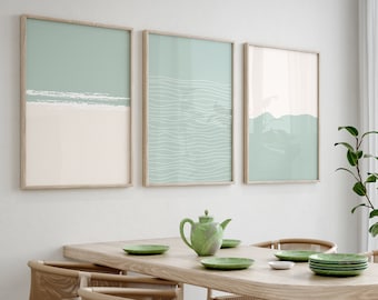 May include: A light wood dining table with a light wood oval tabletop and four woven chairs. The table is set with a green teapot, green plates, and a white saucer. The wall behind the table has three framed prints with a light blue and white abstract design.