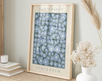 May include: A framed print with a floral design. The print features a pattern of blue flowers on a green background. The title of the print is "FLOWER MARKET" and the location is "STOCKHOLM".