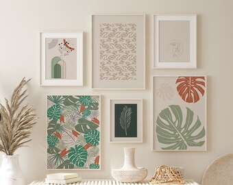 May include: A white wall with six framed prints, including a green and orange tropical leaf print, a green and white leaf print, a brown and white pattern print, a green leaf print, a line drawing of a face, and a line drawing of a plant. The prints are arranged in a grid pattern. There is a white bench with two white wicker baskets underneath the prints.