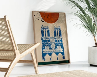 May include: A framed print of Notre Dame Cathedral in Paris, France. The print is in a blue and white color scheme with a brown frame. The print is on a white wall with a wooden chair and a potted plant in the background.