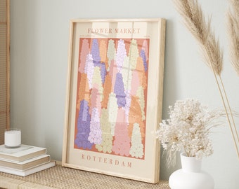 May include: A framed art print featuring a colorful illustration of flowers. The print has a light wood frame and the text "FLOWER MARKET ROTTERDAM" at the top and bottom. The flowers are in shades of purple, orange, pink, and white.