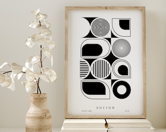 May include: A framed art print featuring a black and white geometric design with the word "RHYTHM". The artwork is in a light wood frame and rests on a stack of books. A wooden vase with decorative branches is in the foreground.