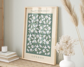 May include: A framed art print featuring a floral design. The print has a light wooden frame and displays a pattern of white flowers on a green background. The words "FLOWER MARKET" and "LONDON" are printed on the artwork.