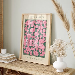 Pode incluir: Um pôster emoldurado com um design floral. O pôster apresenta flores cor-de-rosa sobre um fundo verde. O texto "FLOWER MARKET" e "COPENHAGEN" está impresso no pôster.