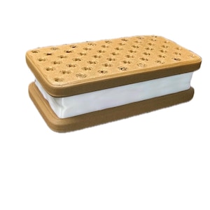 Puede incluir: Un sándwich de helado impreso en 3D de color marrón y blanco. El sándwich está hecho de dos galletas marrones con forma de gofre con un relleno blanco rectangular.