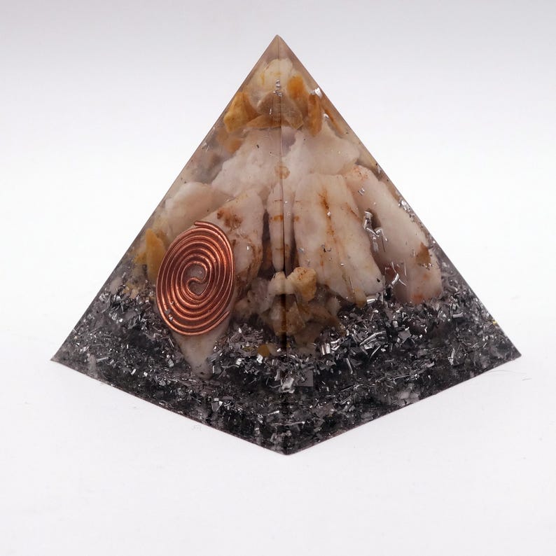 May include: A pyramid-shaped decorative object with a copper coil embedded in the front. The pyramid is made of clear resin, with white and tan stones and dark gray metallic flakes. The pyramid is on a white background.