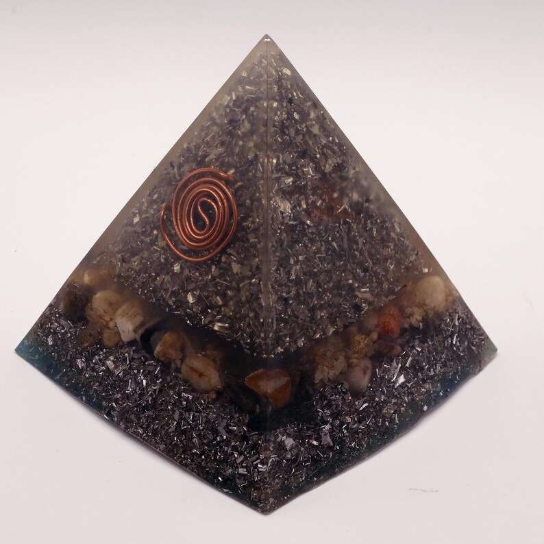 May include: A pyramid-shaped orgone energy generator. The pyramid is made of a clear resin with dark gray and silver inclusions, and small stones. A copper coil is embedded at the top.