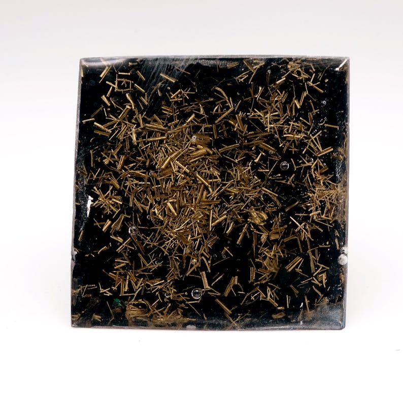 May include: Square, black resin art piece with embedded gold-colored metal shavings. The artwork has a textured appearance with the metallic elements scattered throughout the dark base. The piece is displayed against a white background.