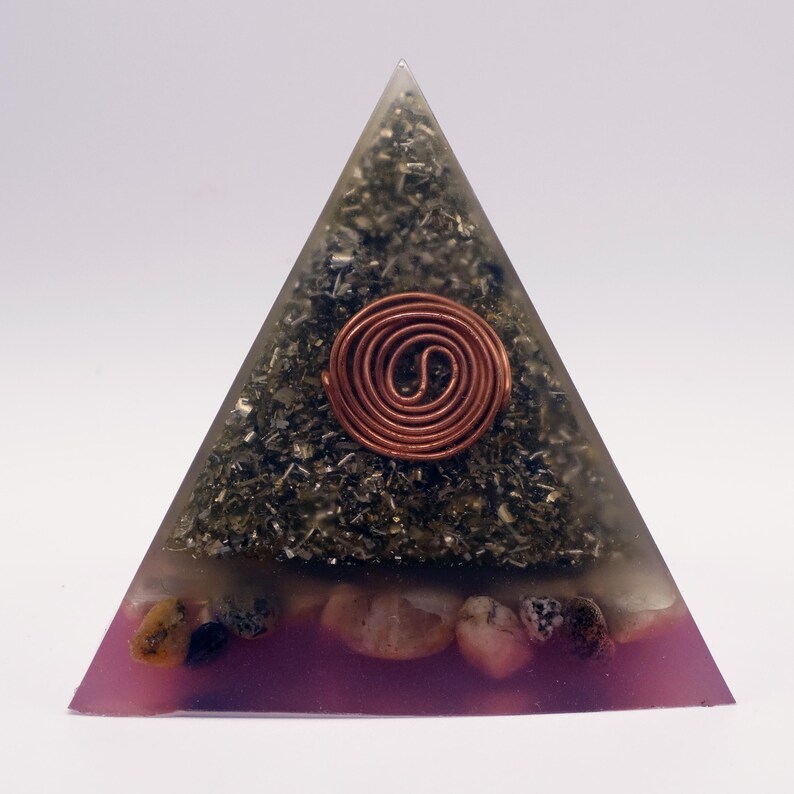 May include: A pyramid-shaped orgone energy generator. The pyramid is clear with a copper coil at the center. The pyramid is filled with dark green and black materials, and a layer of pink resin with small stones at the base.