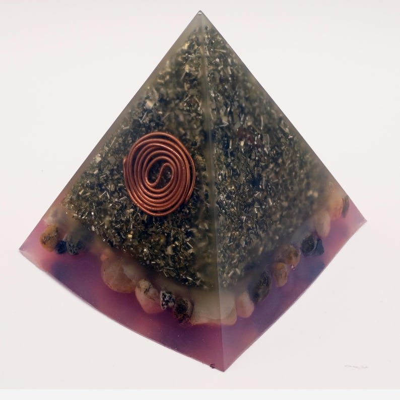 May include: A pyramid-shaped orgone energy generator. The pyramid is made of clear resin with a dark green interior and a copper coil at the center. The base is a translucent purple with small stones embedded around the edges.