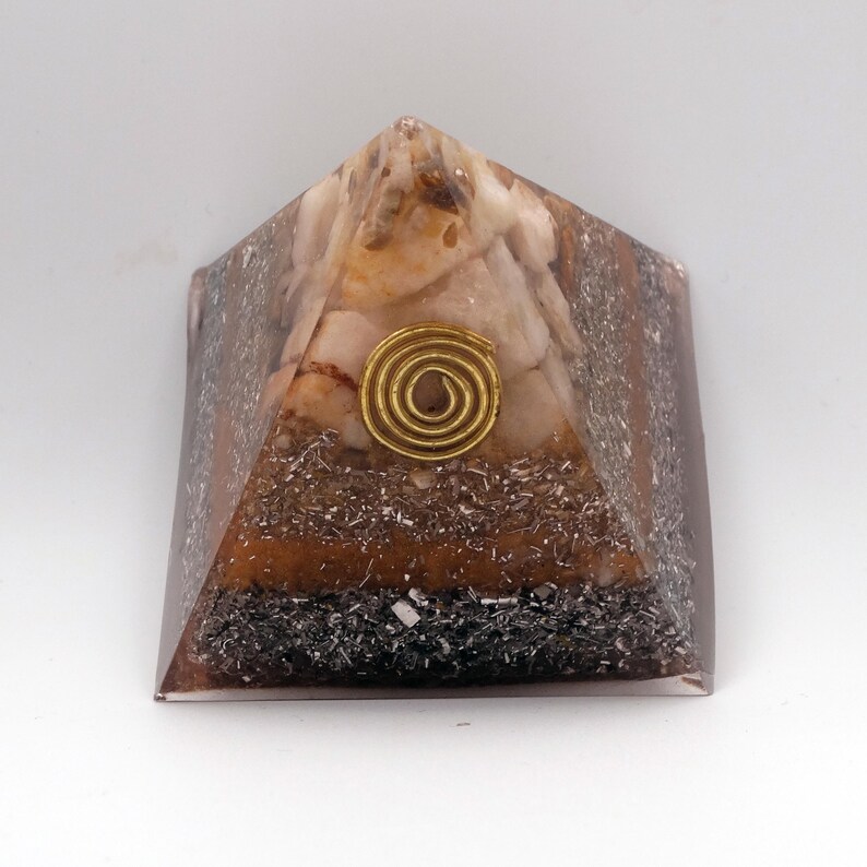 May include: A pyramid-shaped orgone energy generator. The pyramid features a mix of brown, white, and black materials, with a gold-colored spiral at the center. The pyramid is made of resin and is designed to balance energy.
