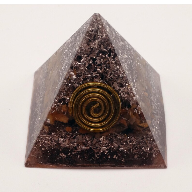 May include: A pyramid-shaped decorative object with a bronze-colored spiral design on the front. The pyramid is made of a translucent material with dark brown and silver-colored inclusions. The base is square.