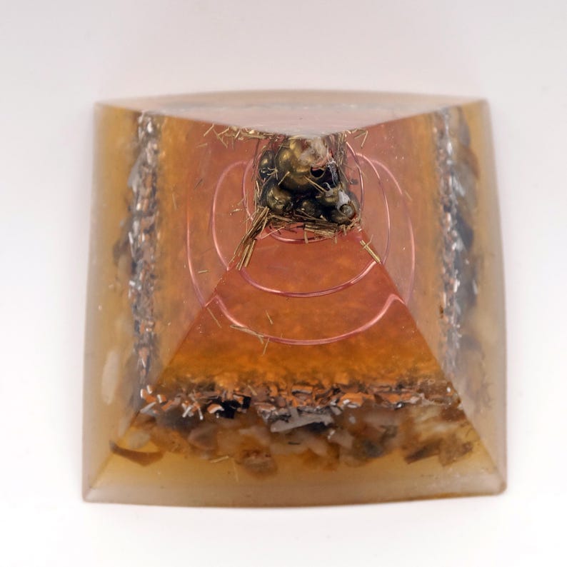 Peut inclure: Une pyramide &agrave; base carr&eacute;e avec un ext&eacute;rieur en r&eacute;sine ambr&eacute;e transparente. &Agrave; l'int&eacute;rieur, des couches de fil de cuivre, des copeaux de m&eacute;tal et un amas d'objets m&eacute;talliques sombres au sommet. La pyramide a un design g&eacute;om&eacute;trique.